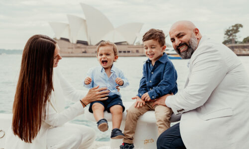 Happy family photos Sydney Opera House session featuring parents and two young boys laughing together by the harbour.