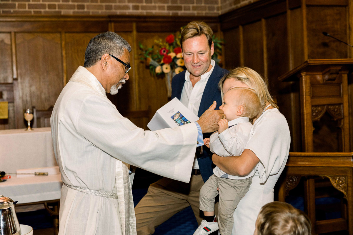 christening photography priest bless the baby boy by touching his nose