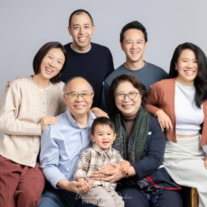 A warm Multigenerational Family Portrait featuring grandparents, parents, and a young child smiling together in a bright studio setting.
