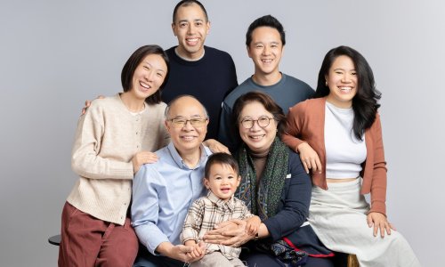 A warm Multigenerational Family Portrait featuring grandparents, parents, and a young child smiling together in a bright studio setting.