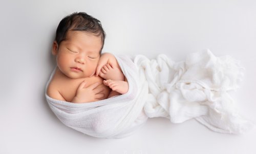 Newborn wrapped in soft white blanket.