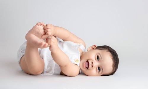 Smiling baby lying on back holding feet during a Sydney Baby Photography session at Blossom Brook Studio.