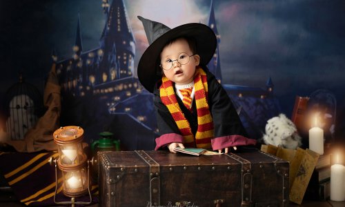 Adorable Harry Potter baby photoshoot with baby Tam wearing glasses, dressed in Gryffindor scarf, and wizard outfit holding a spellbook.