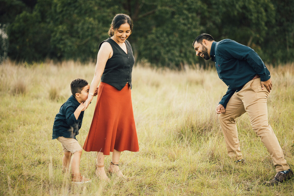 Outdoor Family Photoshoot Sydney at sunset featuring parents smiling with their young son on the father’s shoulders in a golden field.