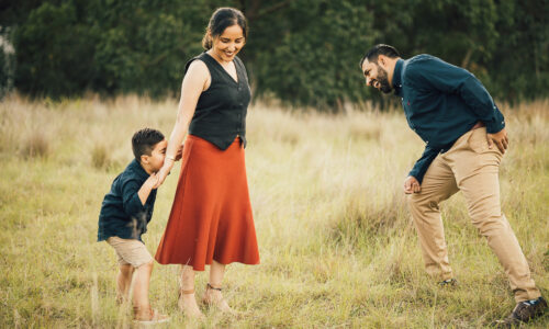 Outdoor Family Photoshoot Sydney at sunset featuring parents smiling with their young son on the father’s shoulders in a golden field.