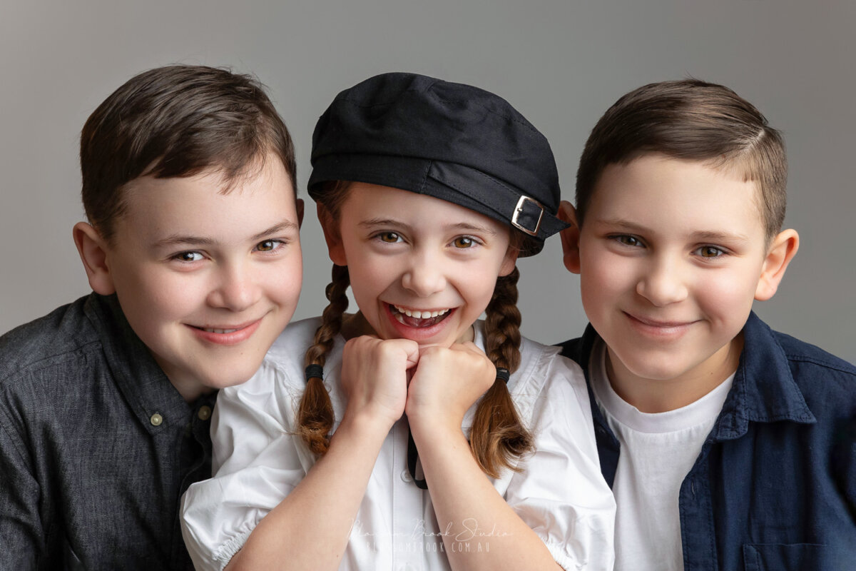 Three happy children smiling in a professional studio portrait, showcasing natural expressions and joyful moments in children photography.