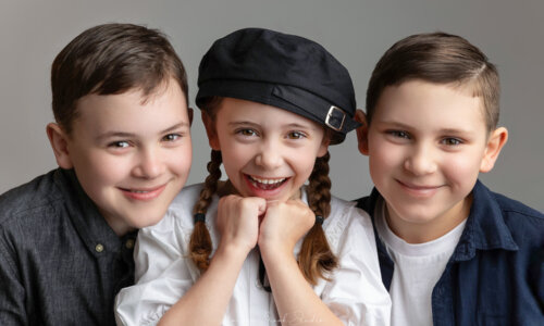 Three happy children smiling in a professional studio portrait, showcasing natural expressions and joyful moments in children photography.