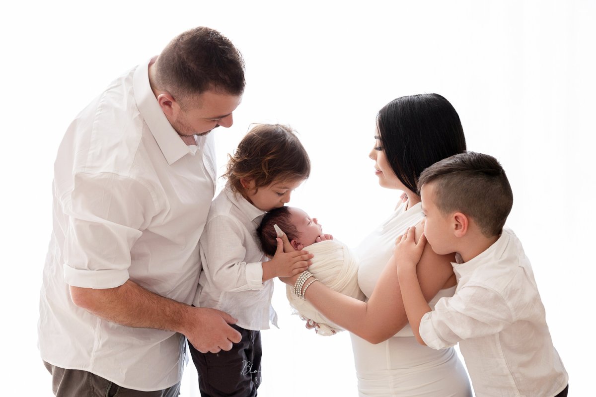Family of five smiling and embracing their newborn baby during a bright, natural-light studio photoshoot in Sydney.
