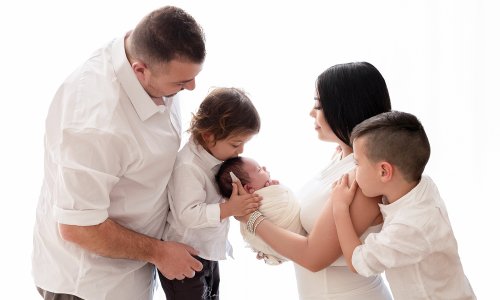 Family of five smiling and embracing their newborn baby during a bright, natural-light studio photoshoot in Sydney.